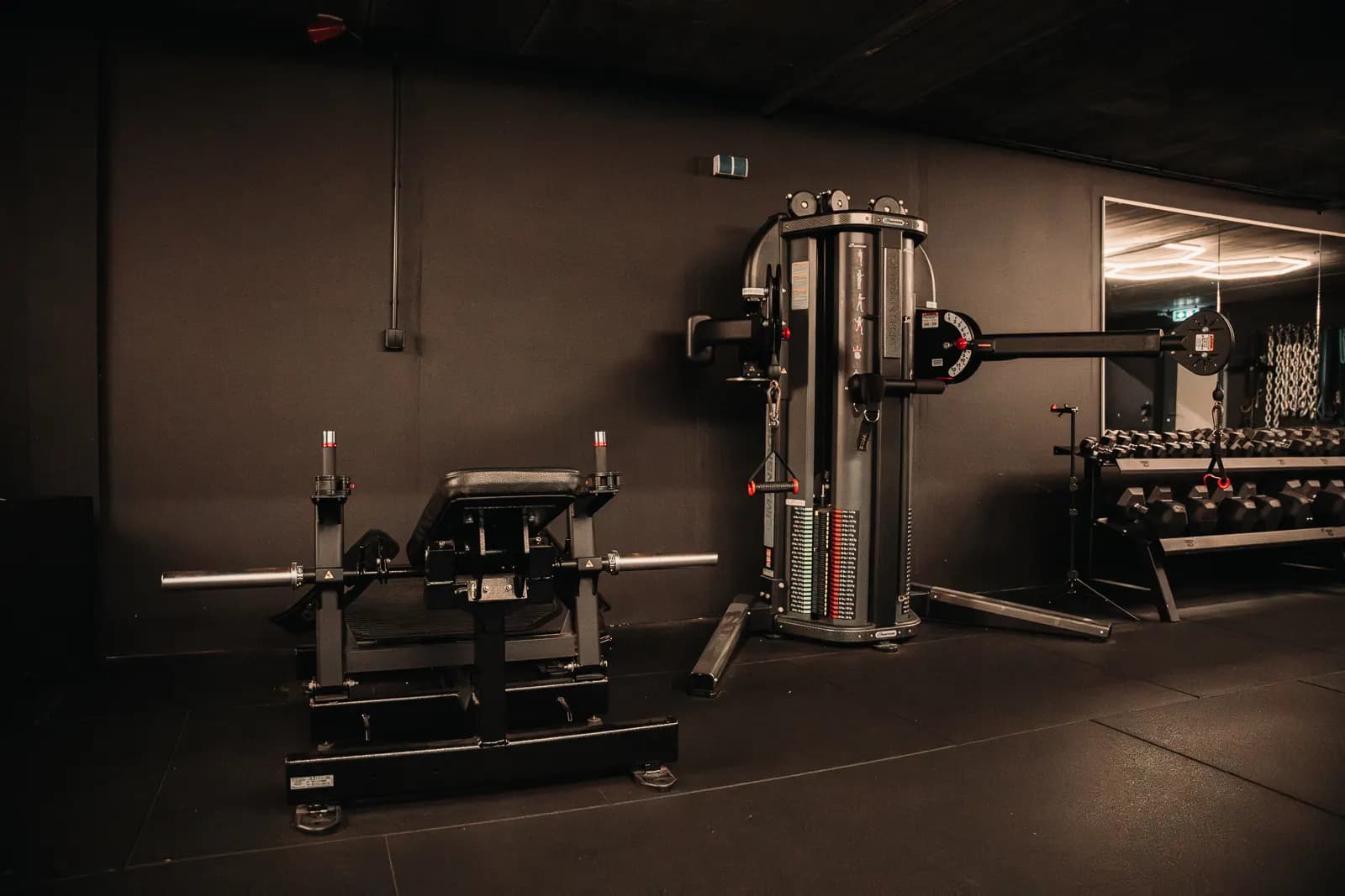 Glute drive en een kabelmachine tegen de zwarte wand van de gym