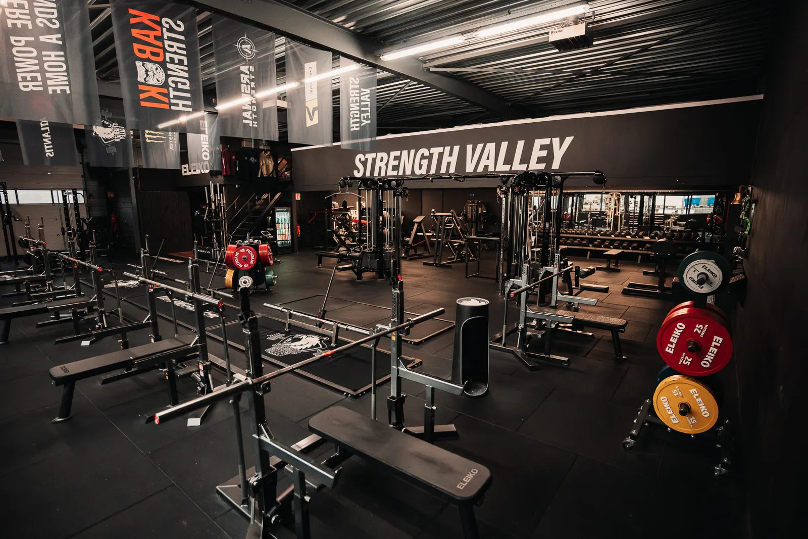 De trainingsvloer van Strength Valley met racks, banken en het opschrift Strength Valley op de wand