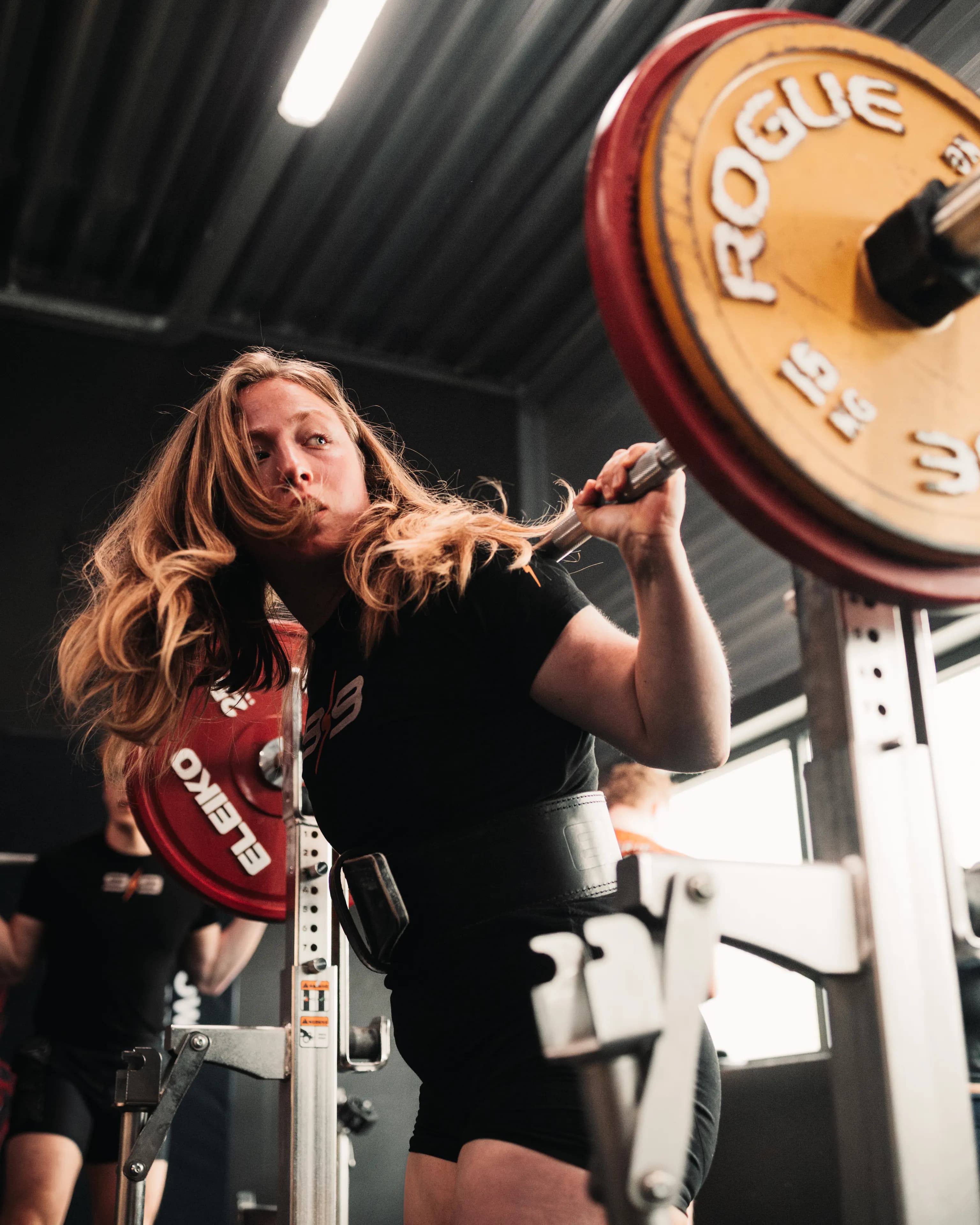 Lifter staat geconcentreerd onder een zwaar beladen stang met Rogue-schijven, klaar voor de squat