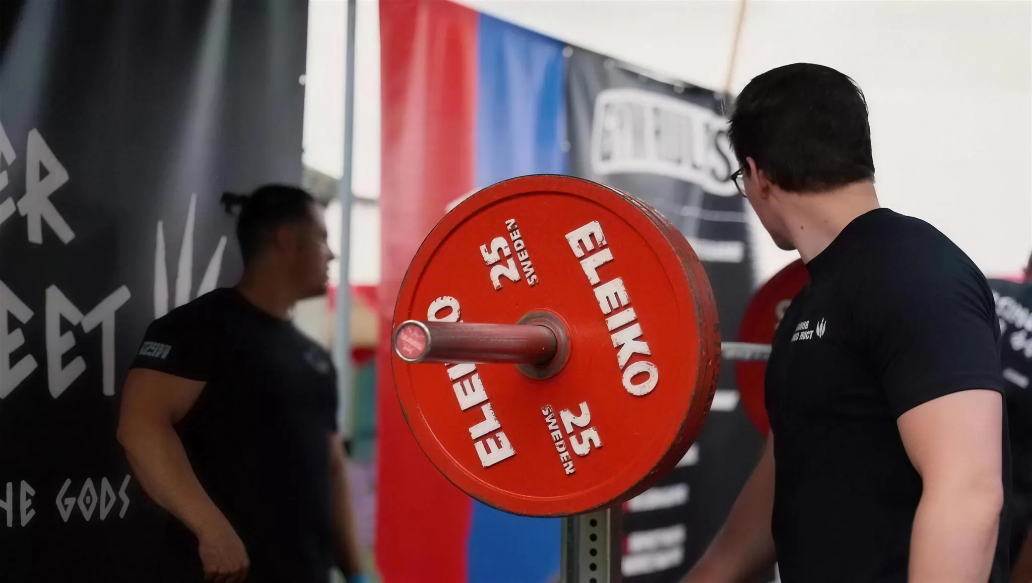 Lifter laadt een rode Eleiko 25 kg-schijf op de stang tijdens een mock meet
